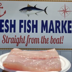 Freshly caught Corvina fillet with fresh fish market sign in the background